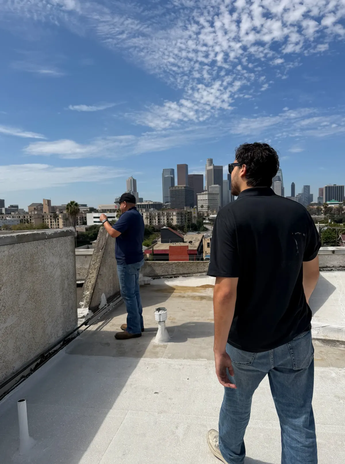Crew inspecting a commercial flat roof with the Los Angeles skyline behind